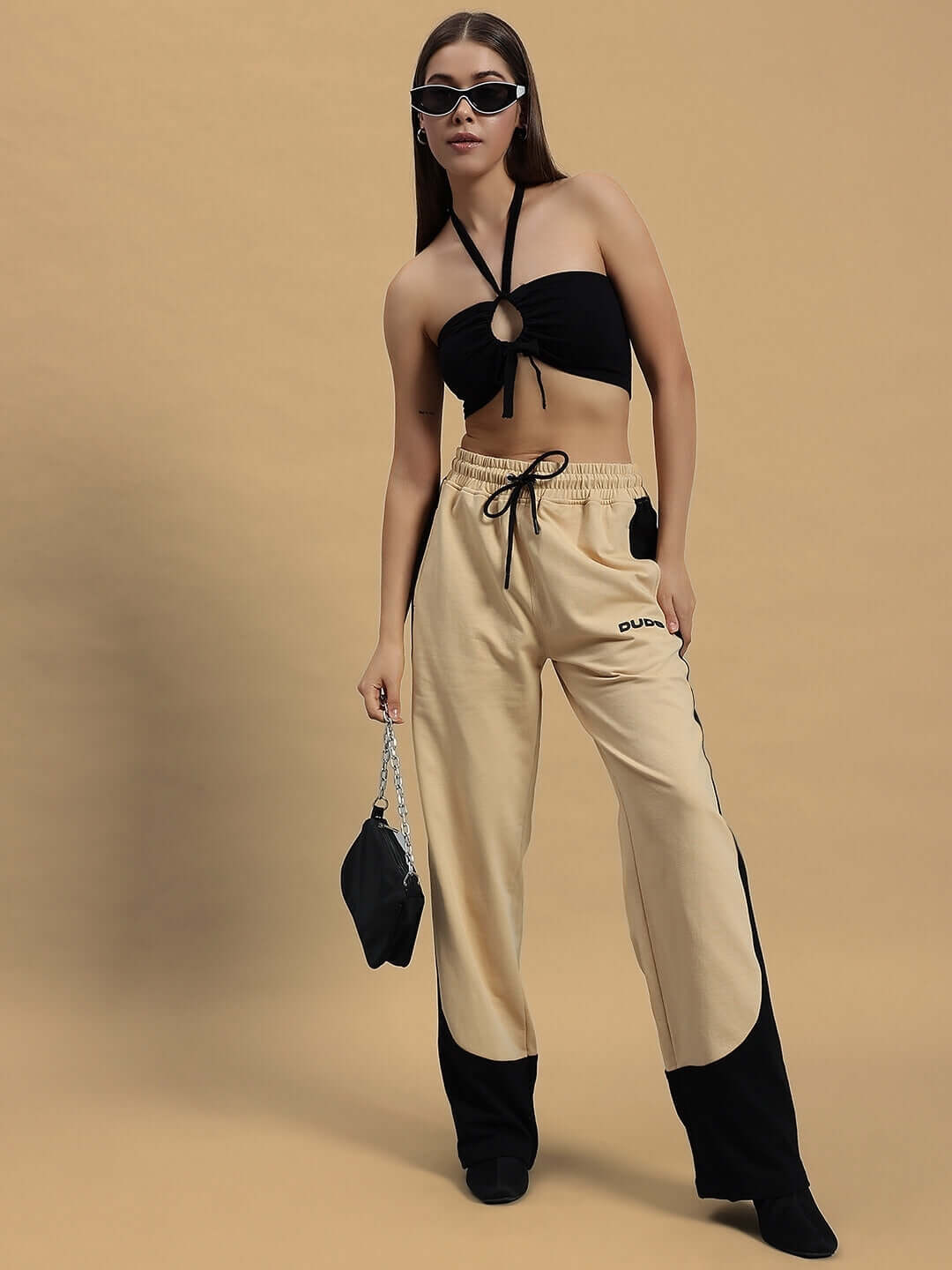 Model wearing Women's Hurtle Baggy Joggers in beige-black paired with a black top and sunglasses, with a black handbag.