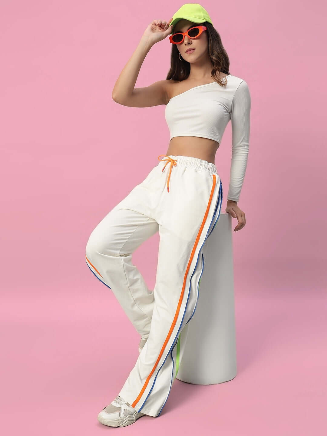 Model wearing women's off-white joggers with side zipper, showcasing sporty design and vibrant stripes, styled with a chic one-shoulder top.
