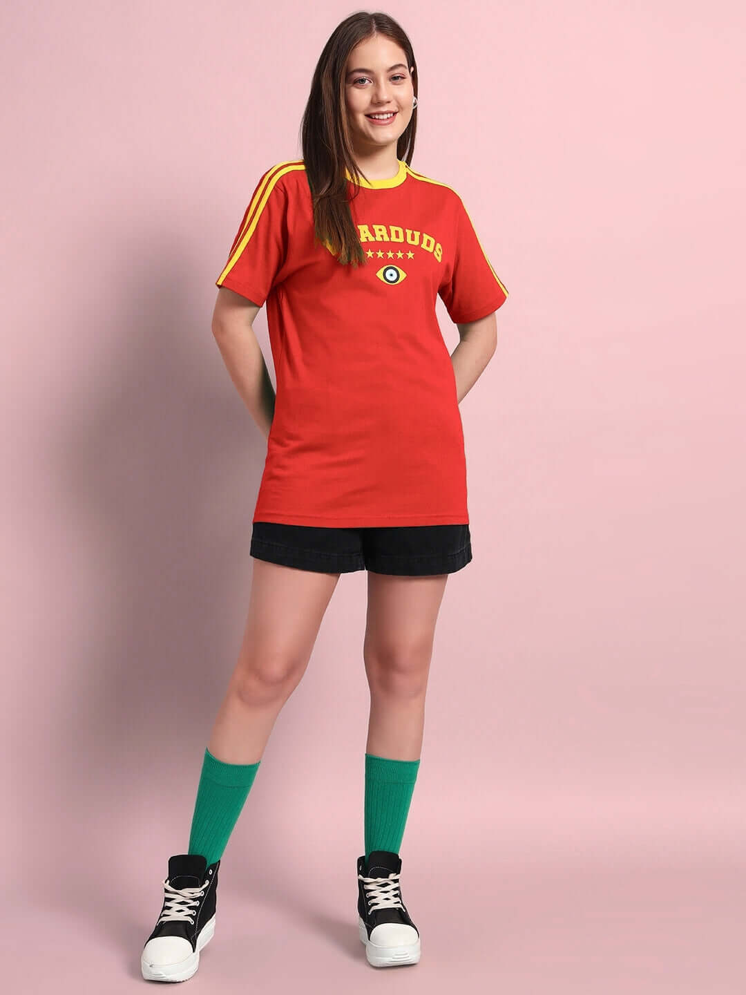 Woman wearing red women's Irish regular fit T-shirt, styled casually with shorts, showcasing vibrant fashion on a pink background.