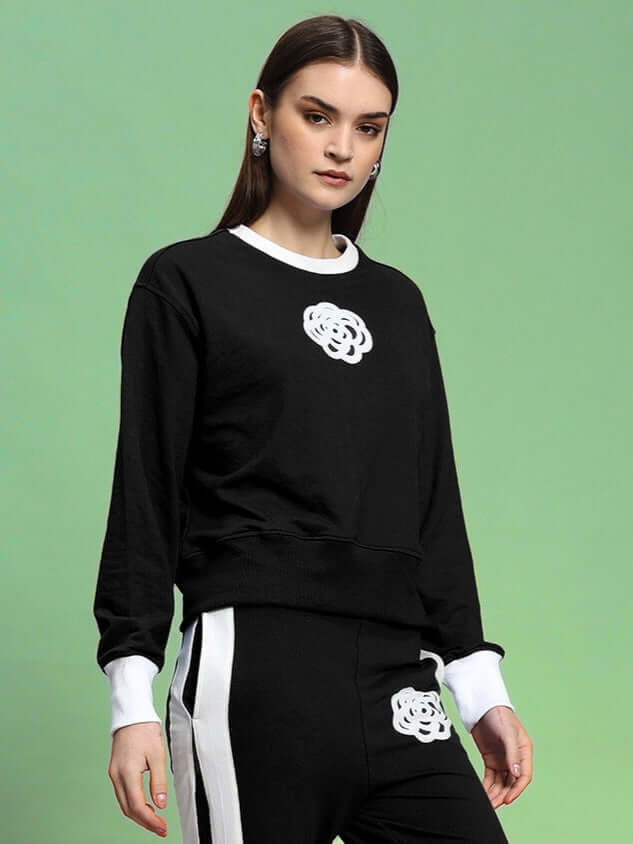 Woman wearing black Jessflick relaxed fit sweatshirt with white accents, premium cotton blend, ideal for casual wear, on a green background.
