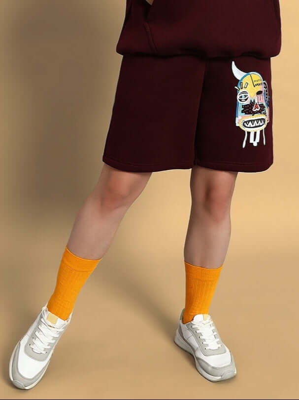 Model wearing WOMEN JUMBLED FLEECE SHORTS WINE with graphic design streetwear look and sneakers, showcasing comfort and style.