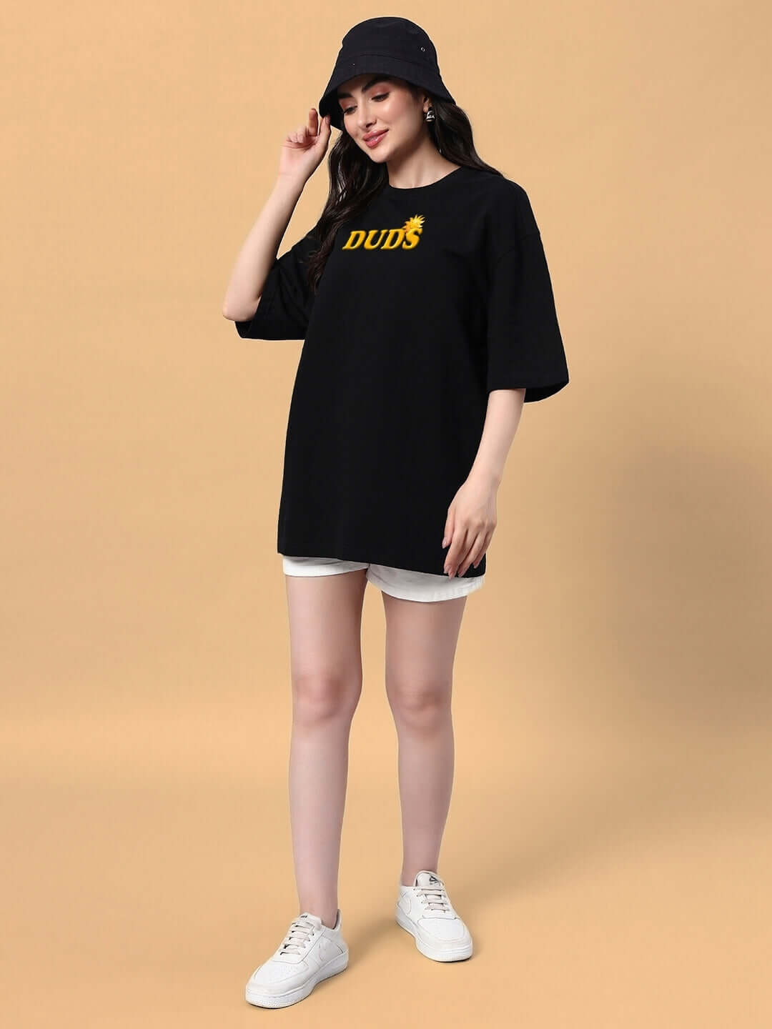 Woman wearing black oversized t-shirt with yellow print, paired with white shorts and sneakers, perfect for a trendy summer look.
