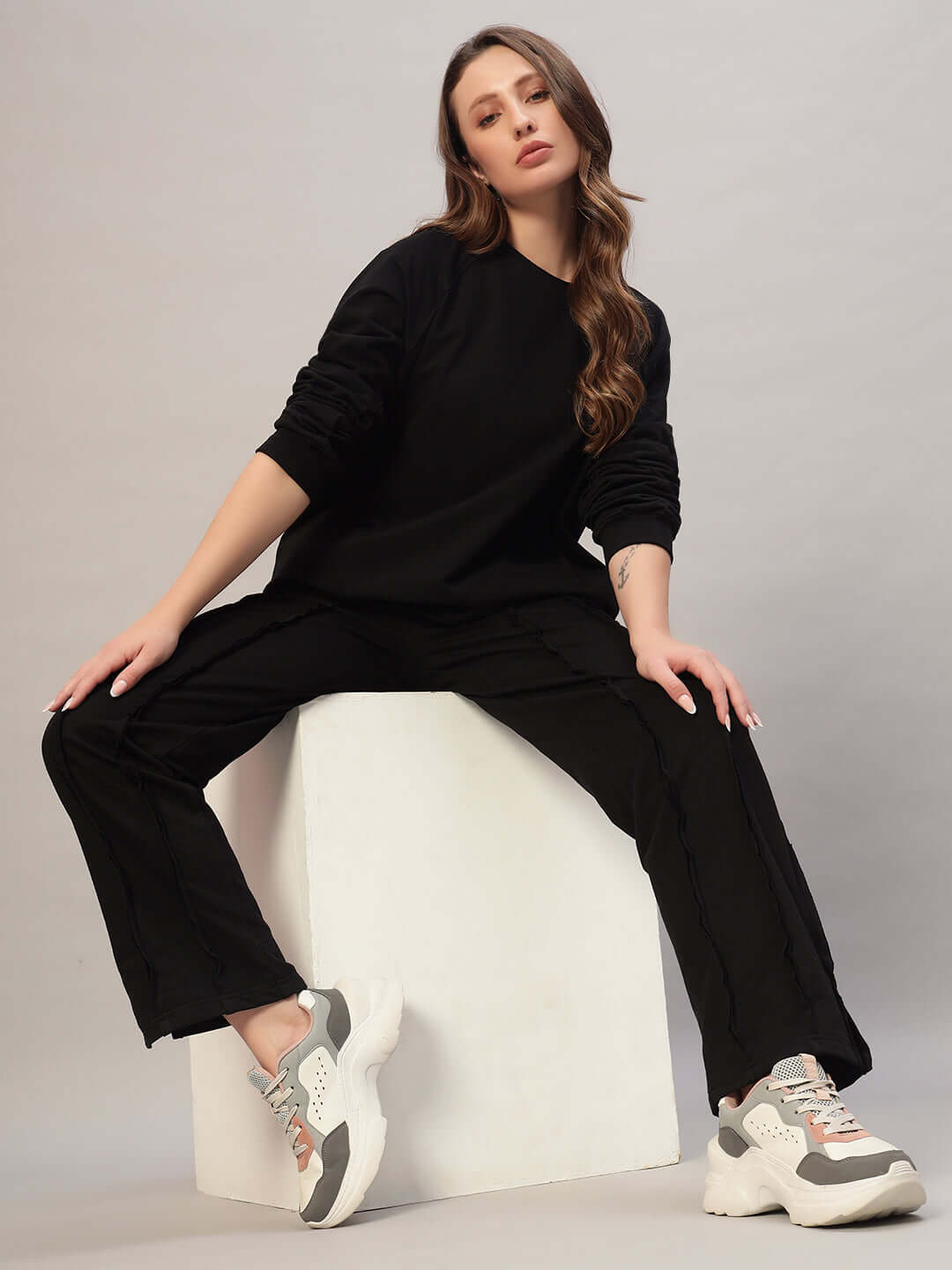 Model wearing women's black oversized co-ord set with relaxed fit joggers, elasticated waistband, and white sneakers.