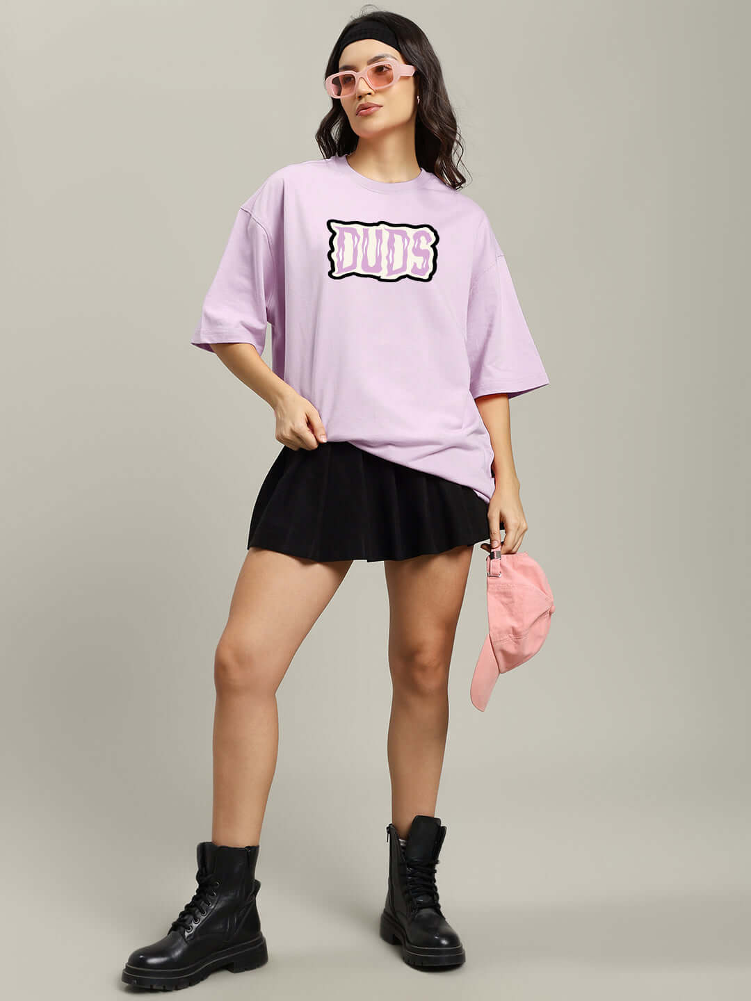 Model wearing lavender oversized 'Let's Get Spooky' T-shirt with skirt and boots, accessorized with pink sunglasses and cap.