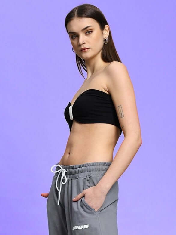 Model wearing WOMEN'S LIA BANDEAU COTTON TOP BLACK, showcasing sleek minimalism and elegance against a purple background.