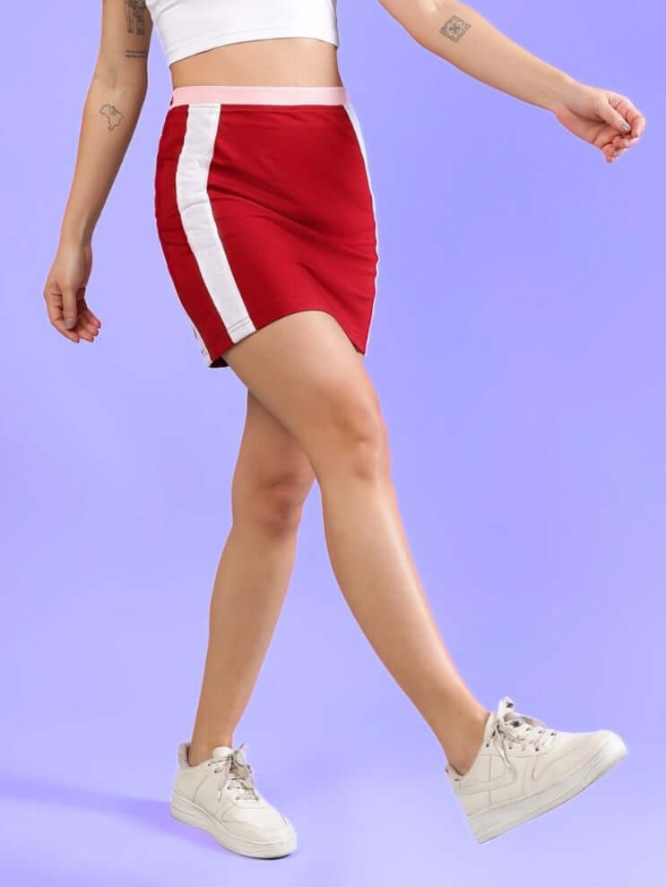 Woman wearing red colorblock skirt with white stripes, walking gracefully against a purple backdrop.
