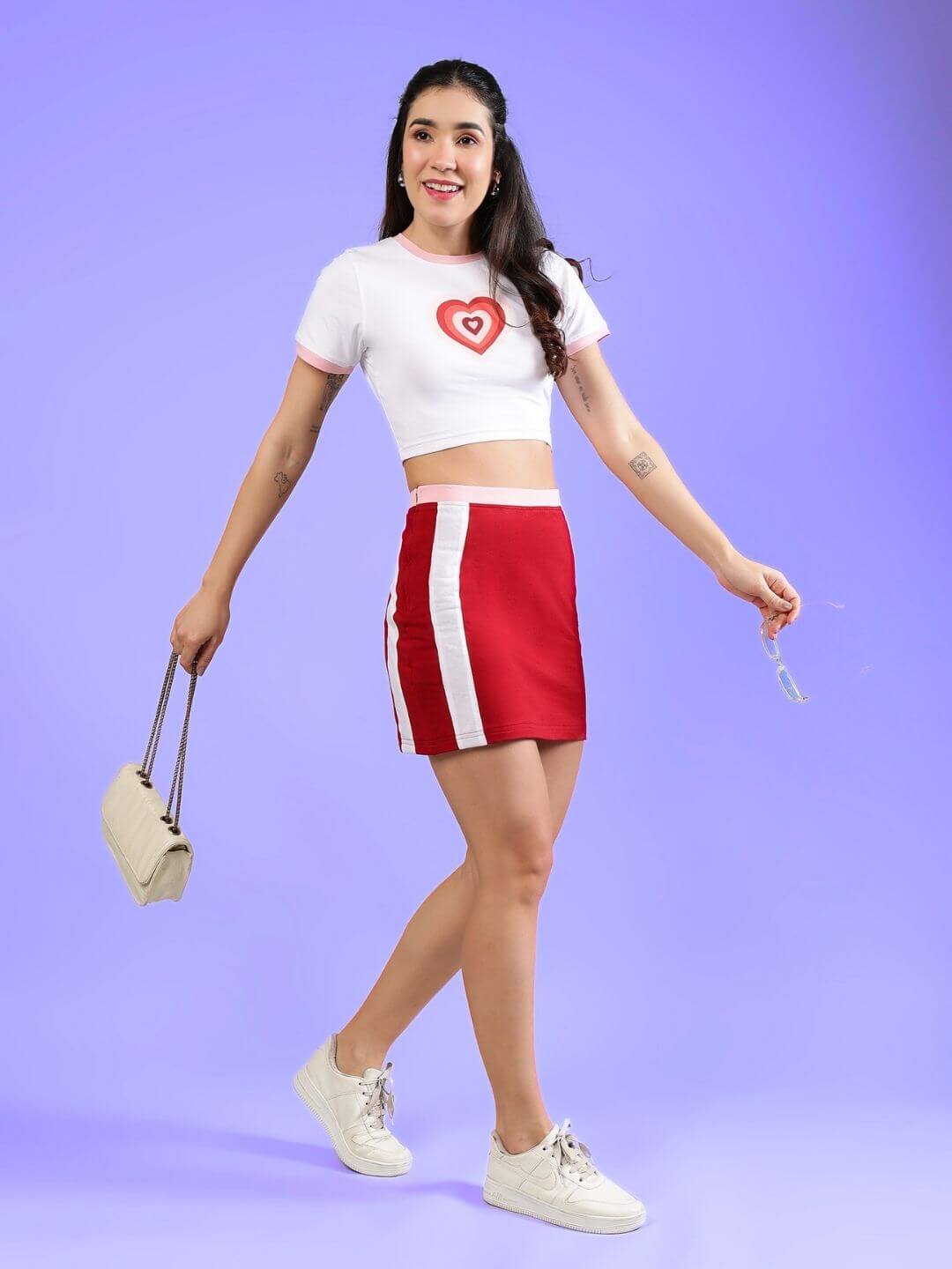 Woman wearing Women's Libi Heart Active Co-ord Set in white and red with heart design, holding a purse on a colorful background.