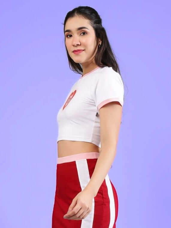 Woman wearing the Women's Libi Heart Crop Top in white, featuring premium cotton fabric and heart detail, against a purple background.