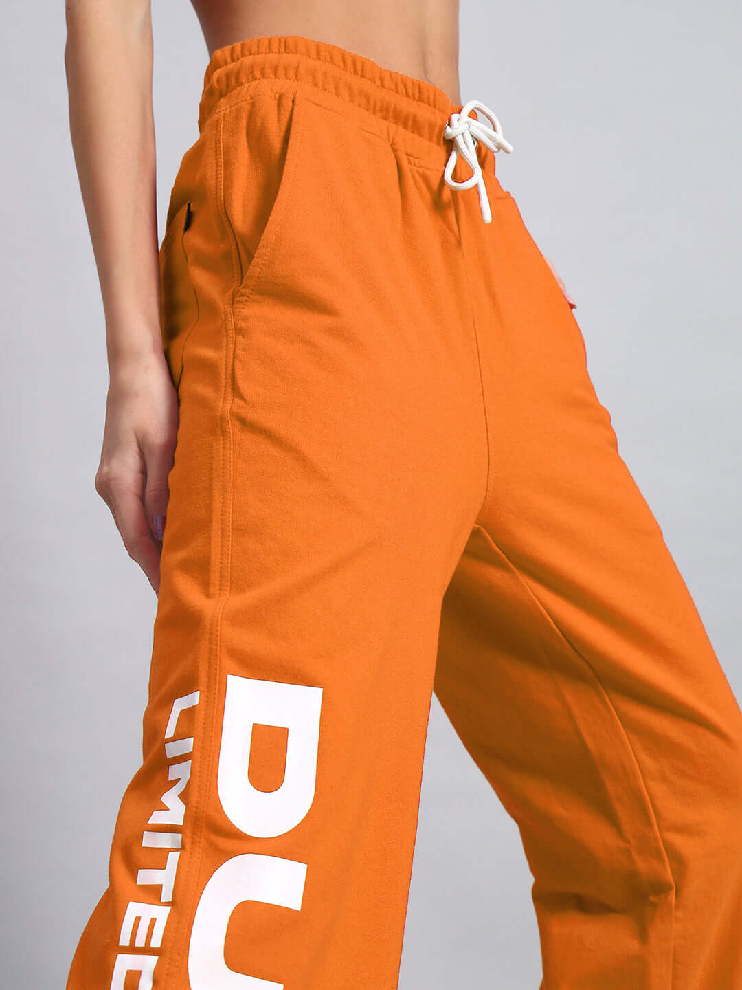 Model wearing WOMEN'S DUDS LIMITED EDITION JOGGER ORANGE with white drawstrings and bold print, side view.