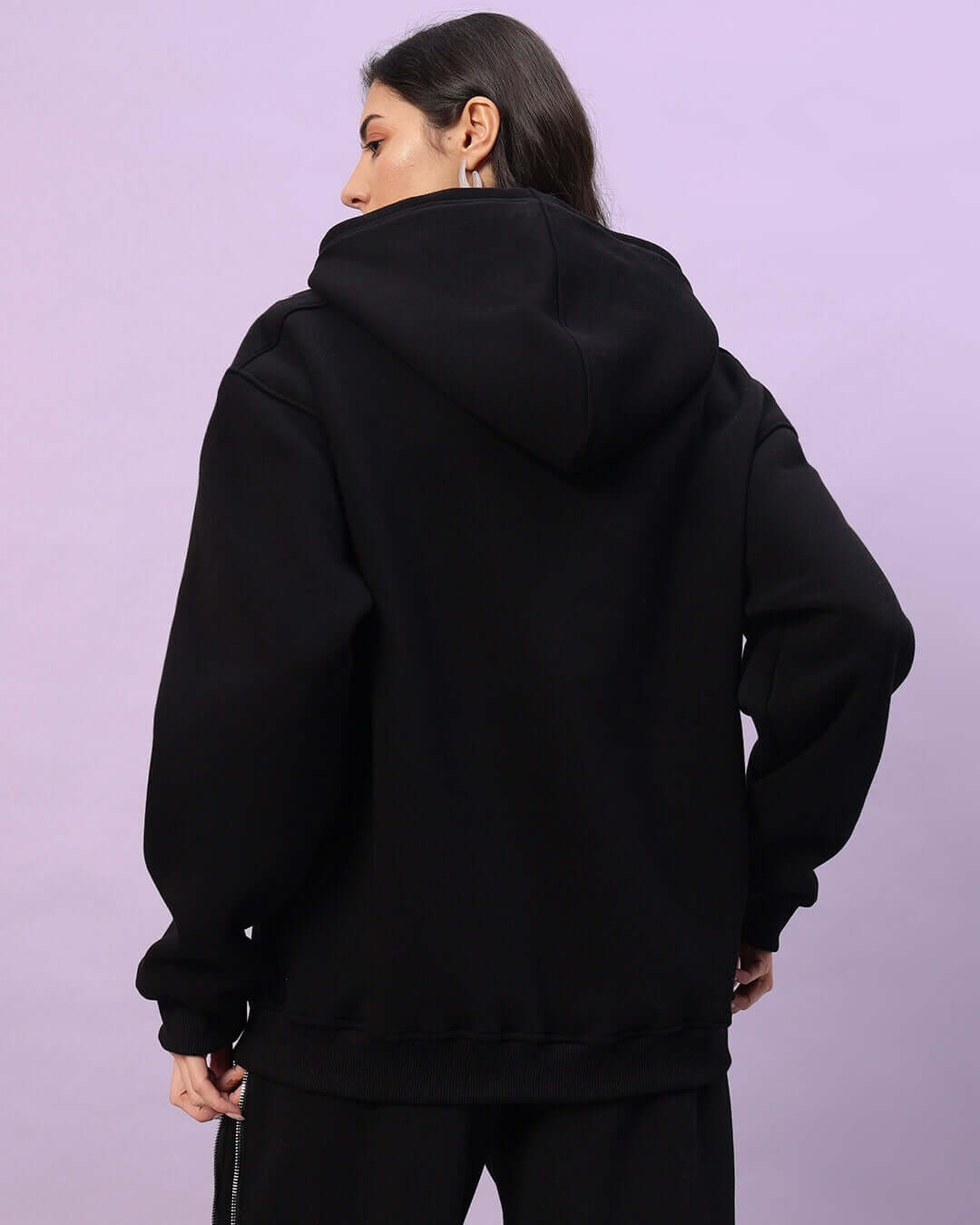 Back view of woman wearing black Limitless Fleece Reflector Hoodie, showcasing comfort and reflector details for stylish safety in low light.