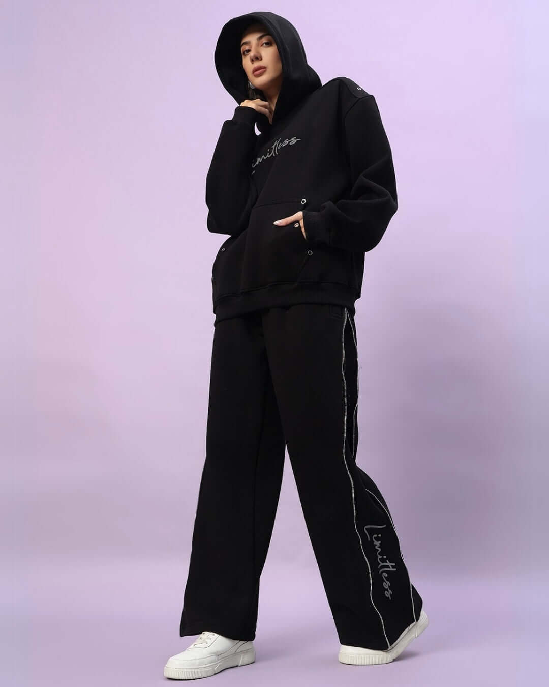 Woman wearing women's Limitless Fleece Reflector Hoodie in black, showcasing modern reflector design, with complementary black pants and white shoes.