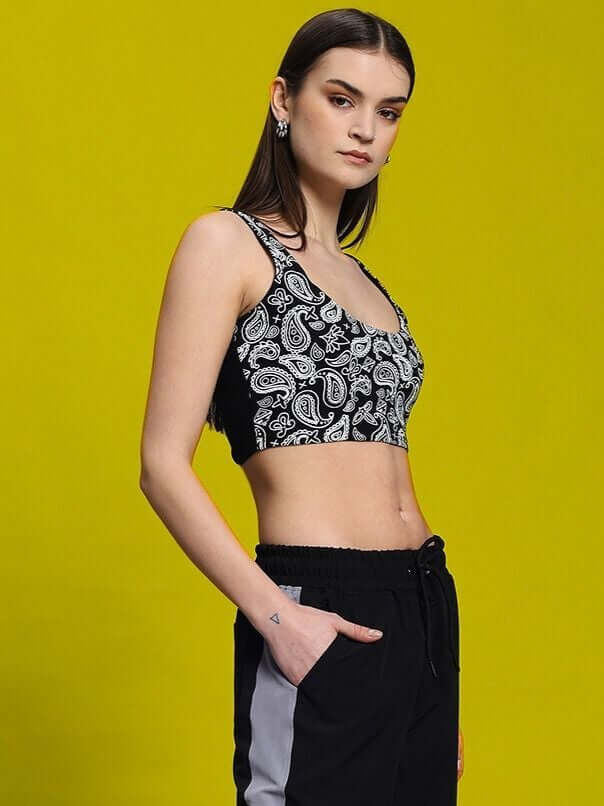 Model wearing women's black crop-top with paisley pattern, styled with black pants, against a yellow background.