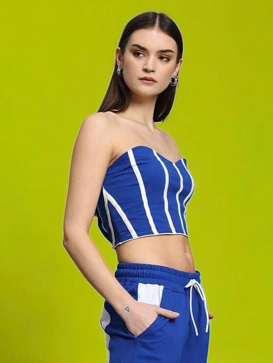 Model wearing WOMEN'S LIVIANA COOL BANDEAU TOP BLUE-WHITE with striped design, showcasing modern coastal style against vibrant background.