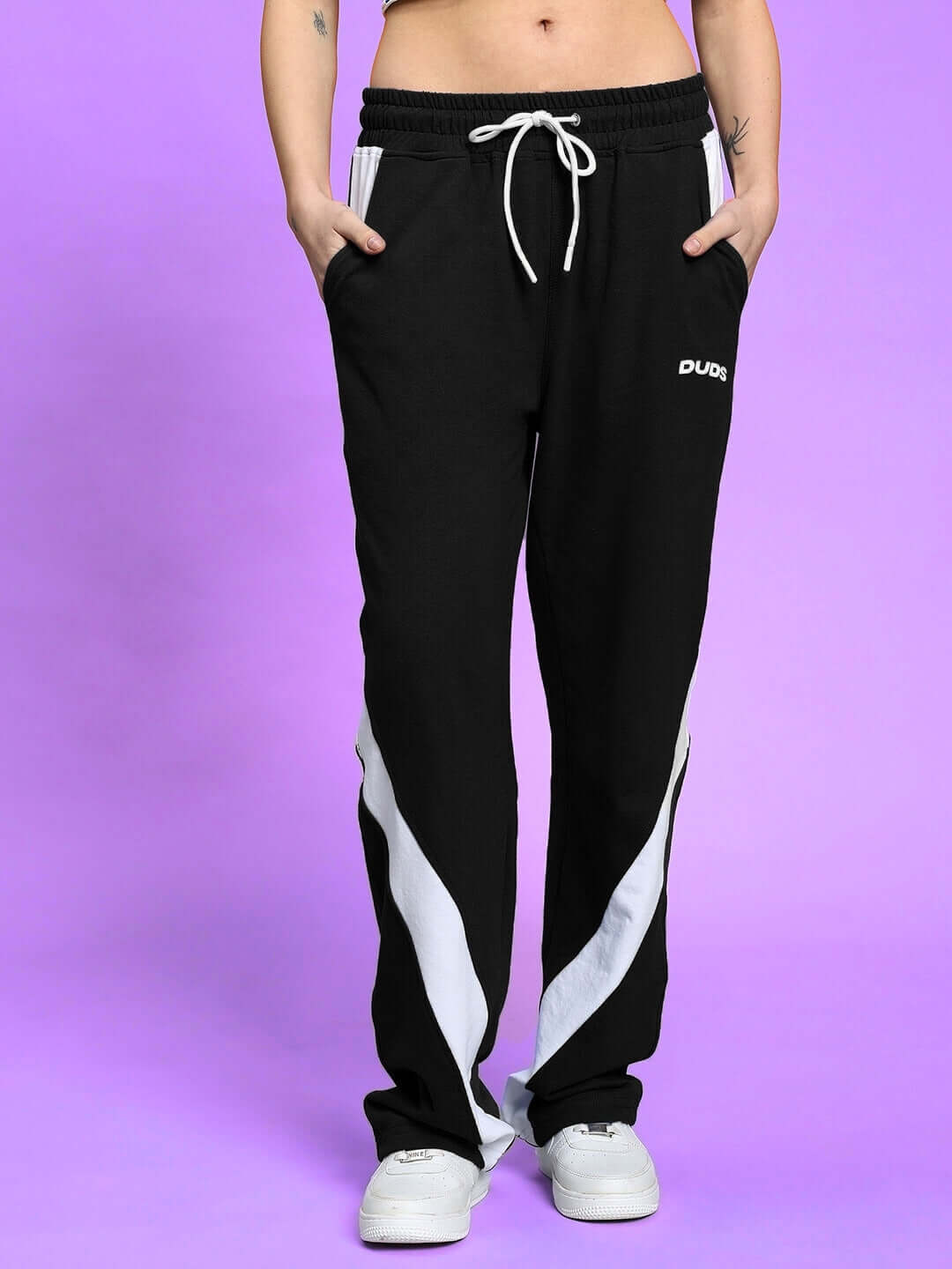 Model wearing WOMEN'S LIVIANA COOL CO-ORD SET BLACK with white sneakers on purple background.