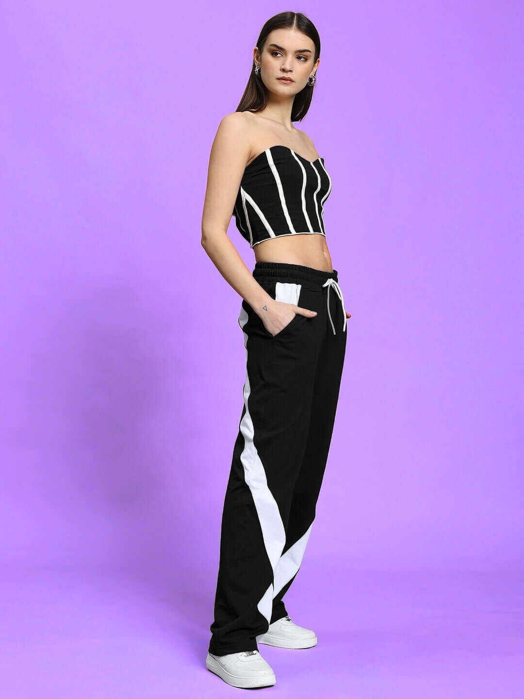 Woman wearing WOMEN'S LIVIANA COOL CO-ORD SET BLACK with striped top and pants, striking a pose on a purple background.
