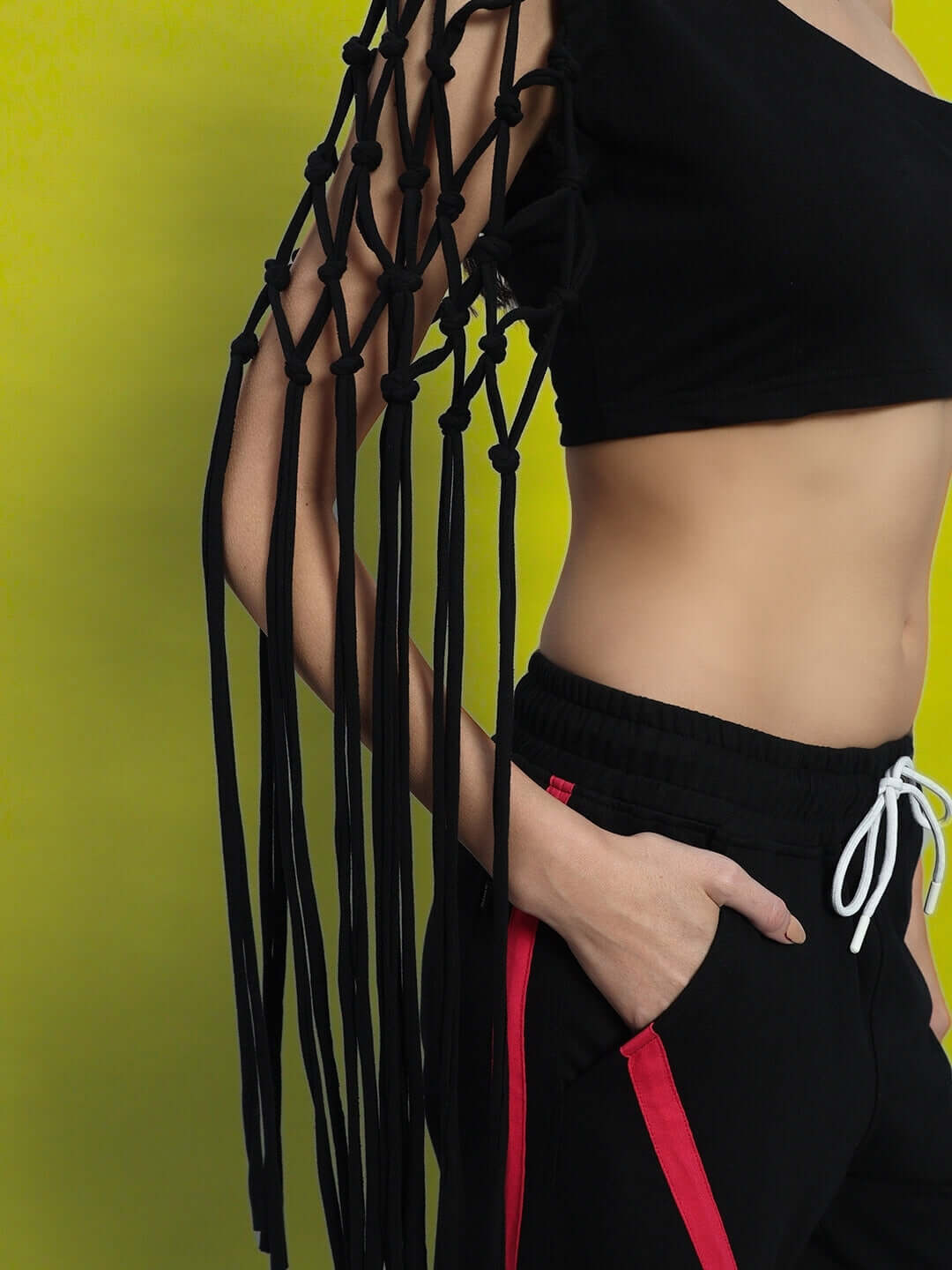 Black women's macrame crop top with fringe sleeve details, made from premium 100% cotton lycra, photographed against a yellow background.
