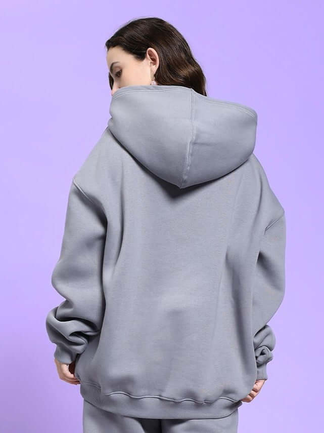 Back view of WOMEN'S MAKE IT HAPPEN FLEECE HOODIE GREY worn by a woman on a purple background