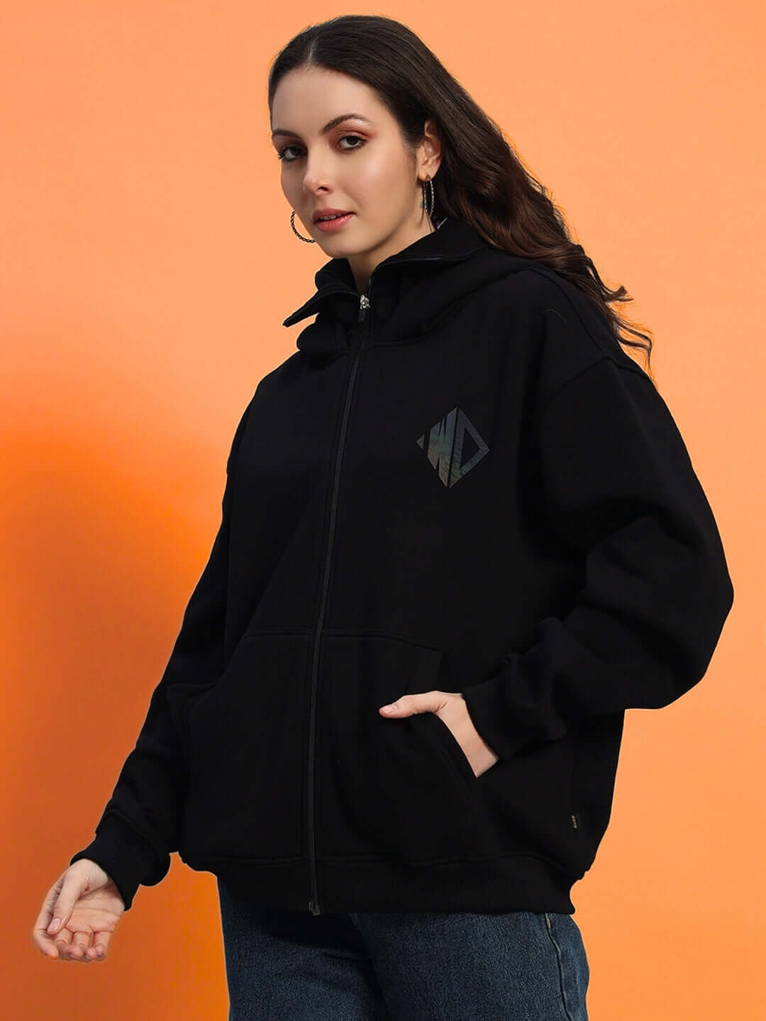 Woman wearing oversized black fleece hoodie with graphic logo, featuring front pockets and full zip closure.