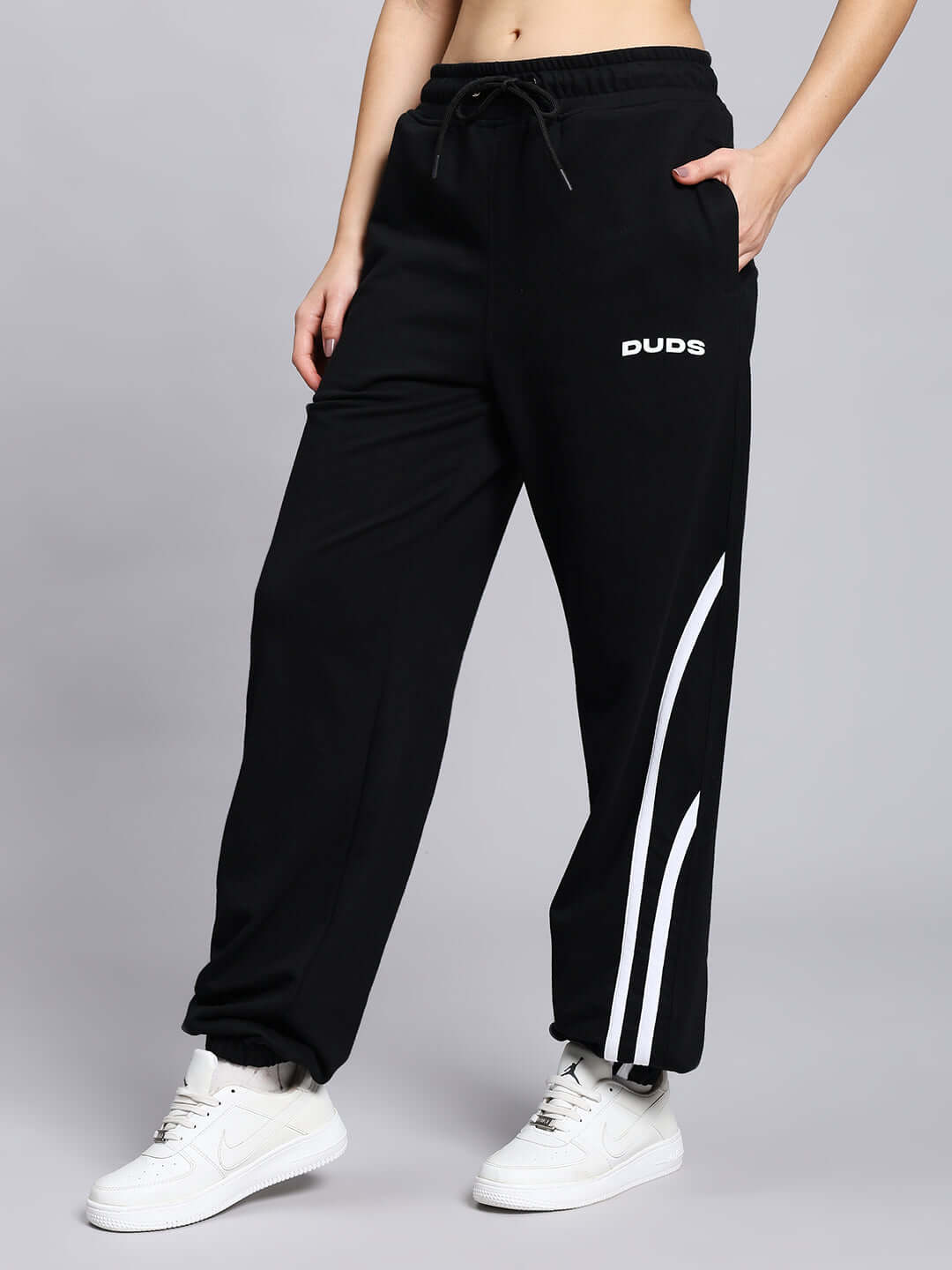 Woman wearing black Megastar 2 Stripe Jogger with custom fit option by DUDS, featuring white stripes and sneakers, 7-10 day dispatch.