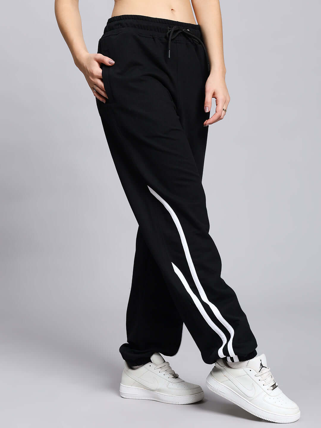 Woman wearing black jogger pants with white stripes, showcasing the Women's Megastar 2 Stripe Jogger. Stylish and comfortable fit.