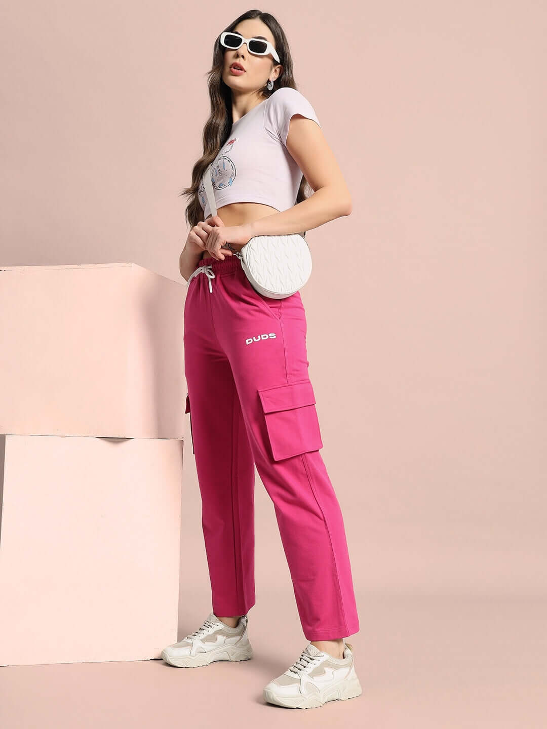 Woman wearing pink Women's Merriam Joggers from DUDS, styled with a white cropped top and sneakers, posing against a neutral background.