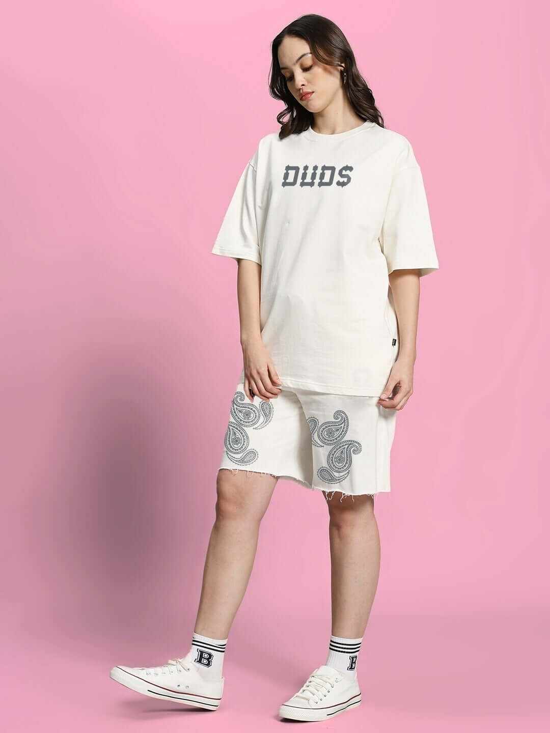 Model wearing WOMEN'S MESSI PAISLEY PRINT CO-ORD SET OFF WHITE with oversized t-shirt and paisley shorts on pink background.