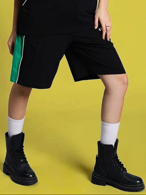 Women's black regular fit shorts with green stripe, custom size options, paired with black boots on a yellow background.
