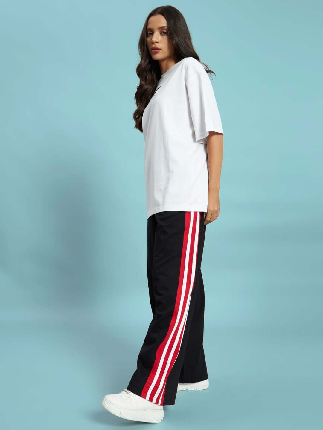 WOMEN'S MILANO RELAXED-FIT JOGGERS BLACK-RED Woman wearing black-red Milano relaxed-fit joggers from DUDS against blue background, showcasing side stripes and comfortable fit.