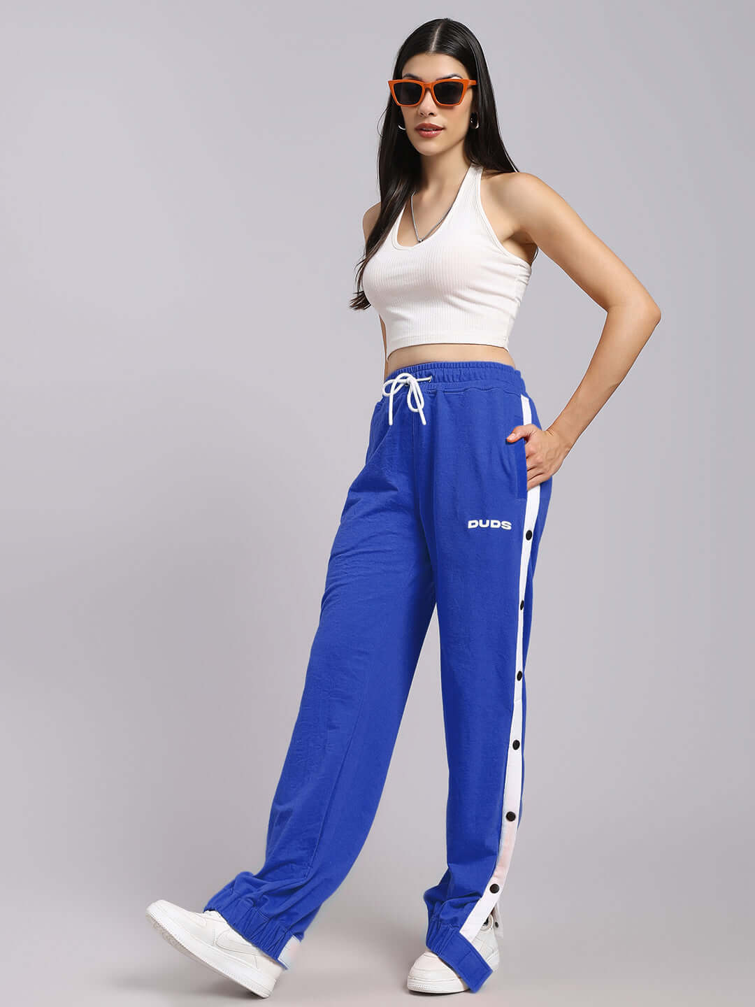 Model wearing DUDS Women's Miller Relaxed Fit Joggers in blue, designed with side stripes and a comfortable drawstring waist.