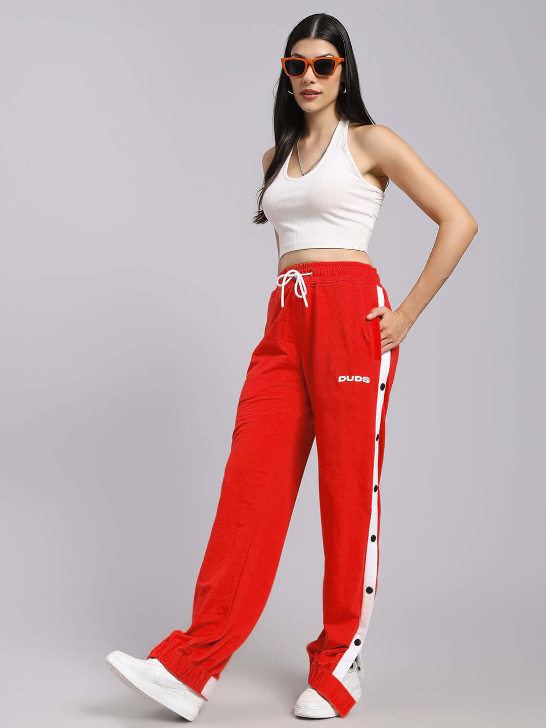 Model wearing women's red relaxed fit joggers from DUDS, paired with a white top and sunglasses.