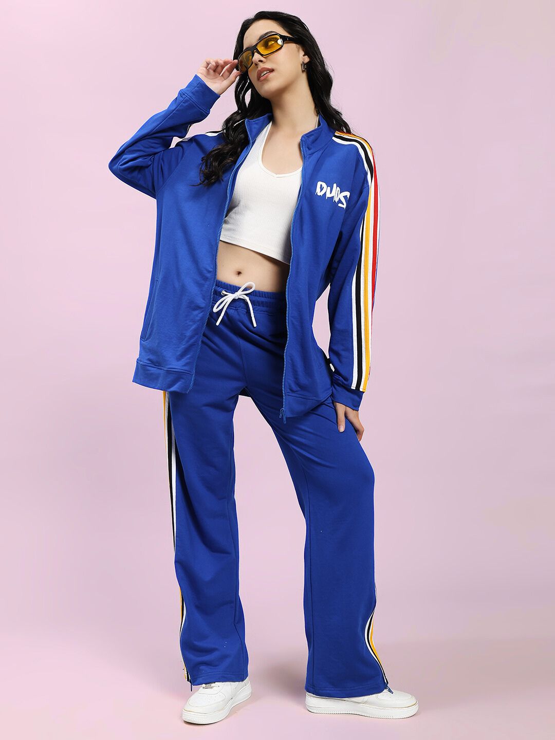 Woman wearing WOMEN MODERN EDGE MULTI-STRIPE JACKET ROYAL BLUE with matching pants against pink background.