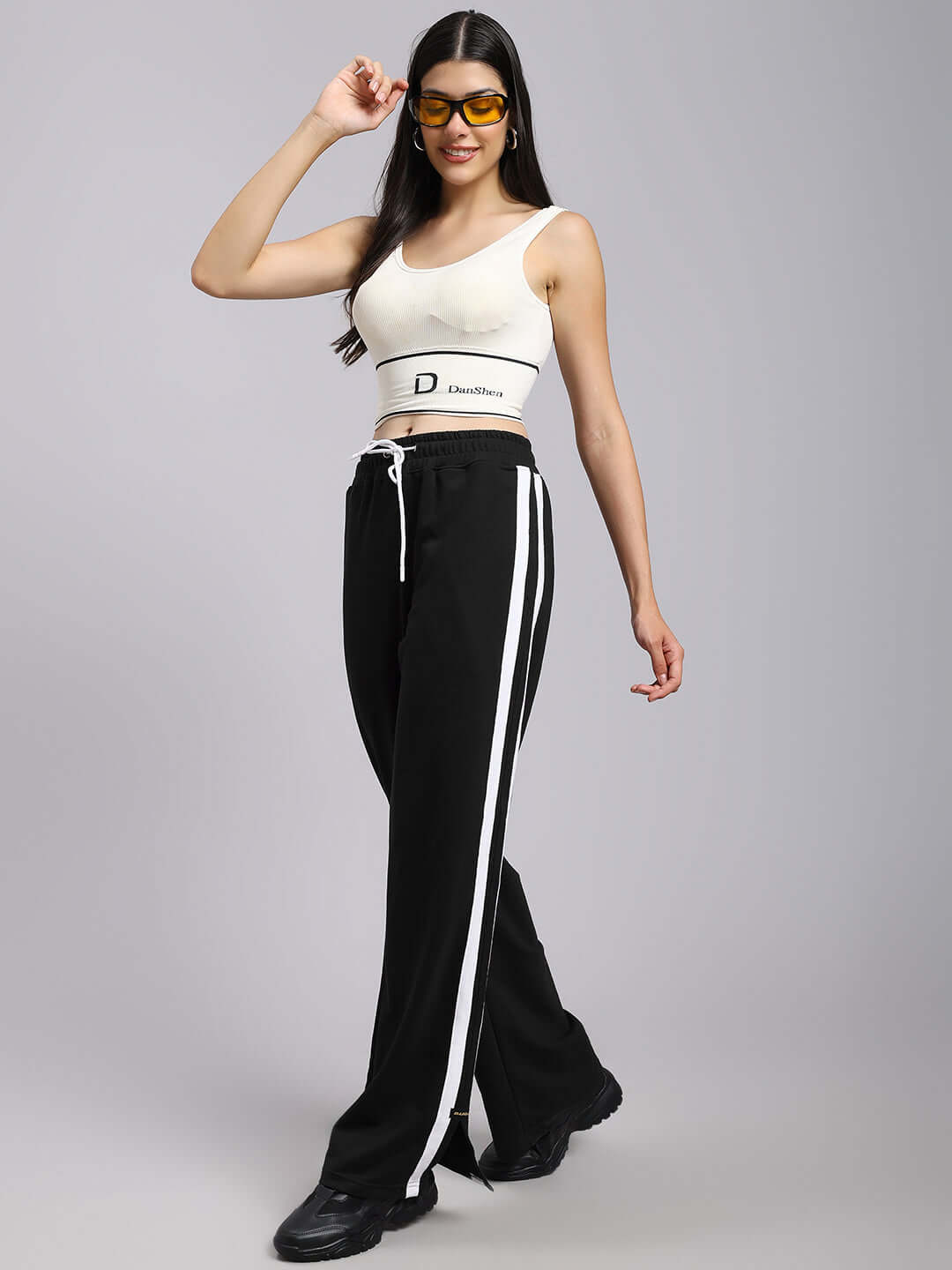 Model wearing women's black relaxed fit joggers with white stripes, styled with a cream top and sunglasses.