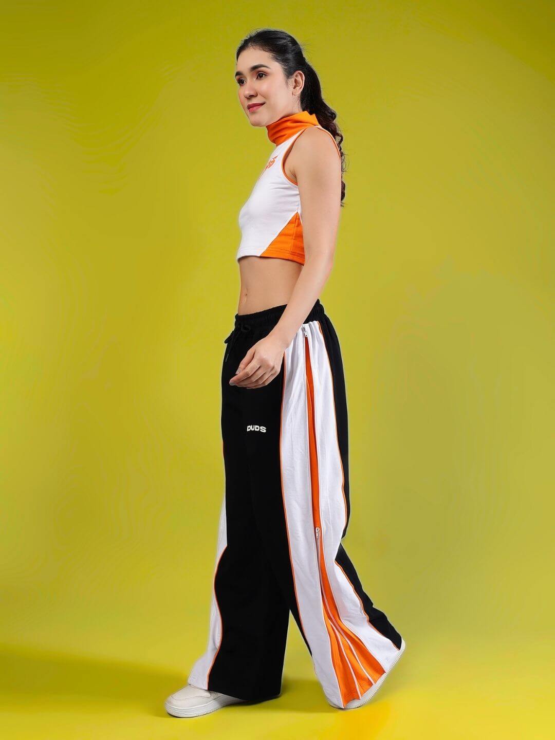 Model wearing WOMEN'S MYSKY CO-ORD SET WHITE BLACK ORANGE from WEAR DUDS, showcasing vibrant streetwear fashion against a yellow background.