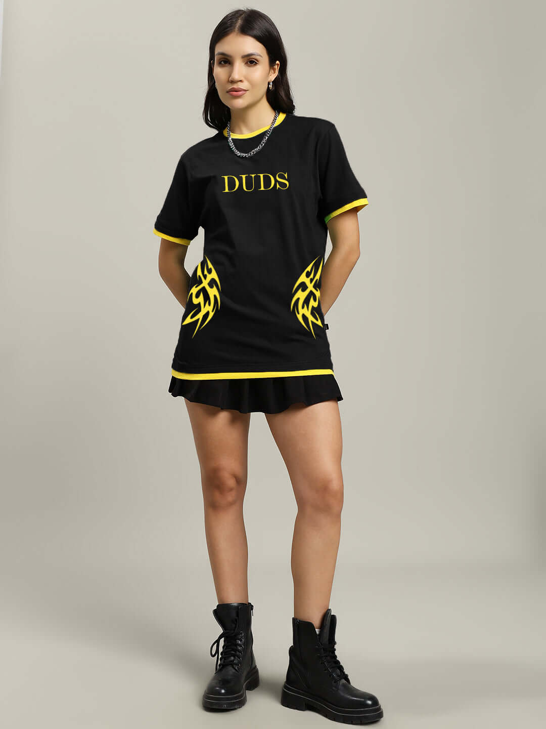 Woman wearing black t-shirt with yellow flame design and branding, paired with black boots against a neutral background.