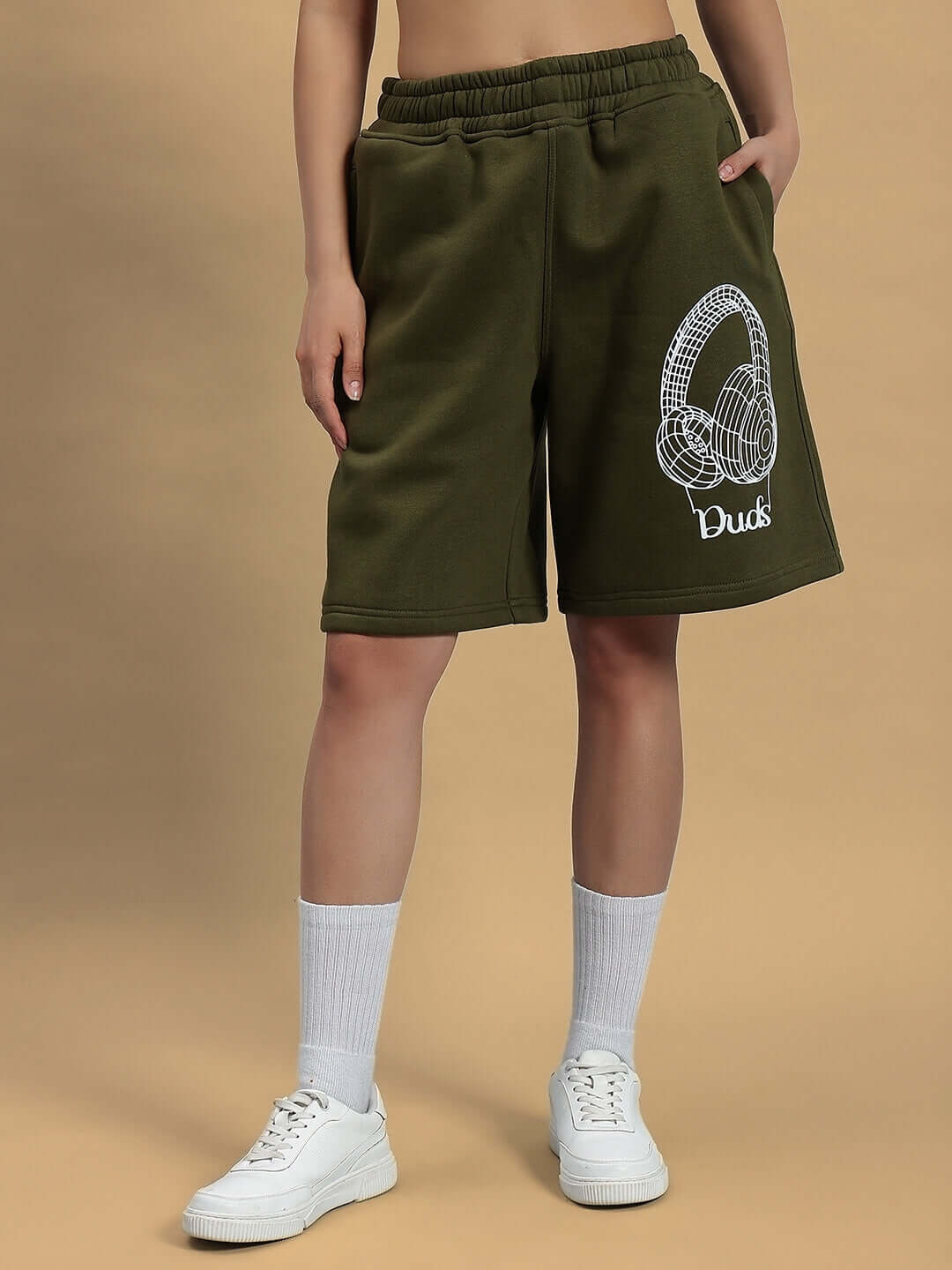 Model wearing WOMEN OPERA FLEECE CO-ORD OLIVE GREEN shorts with white sneakers on beige background.