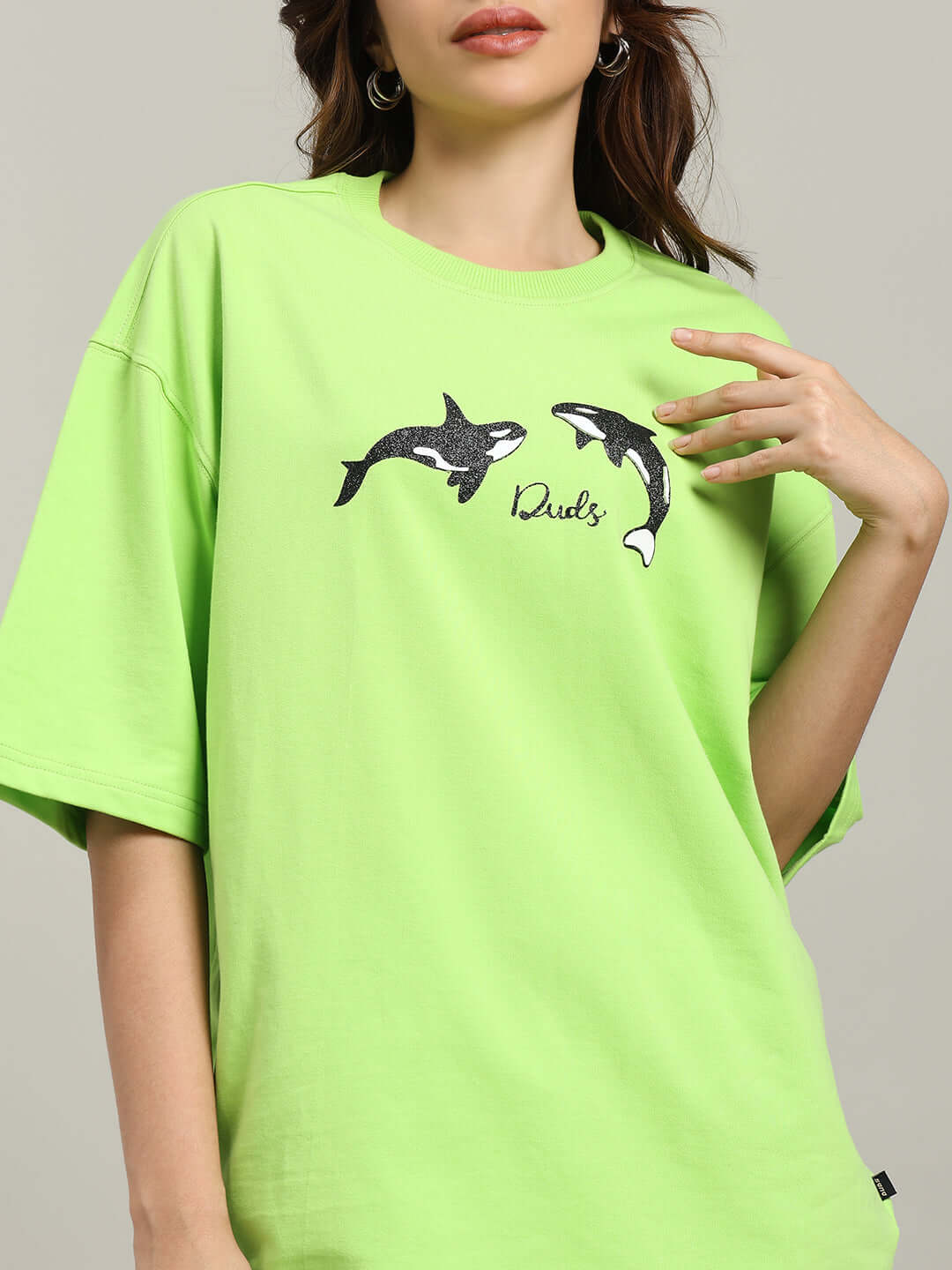 Woman wearing WOMEN'S ORCAS OVER-SIZED T-SHIRT NEON GREEN with orca graphics, showcasing streetwear style.