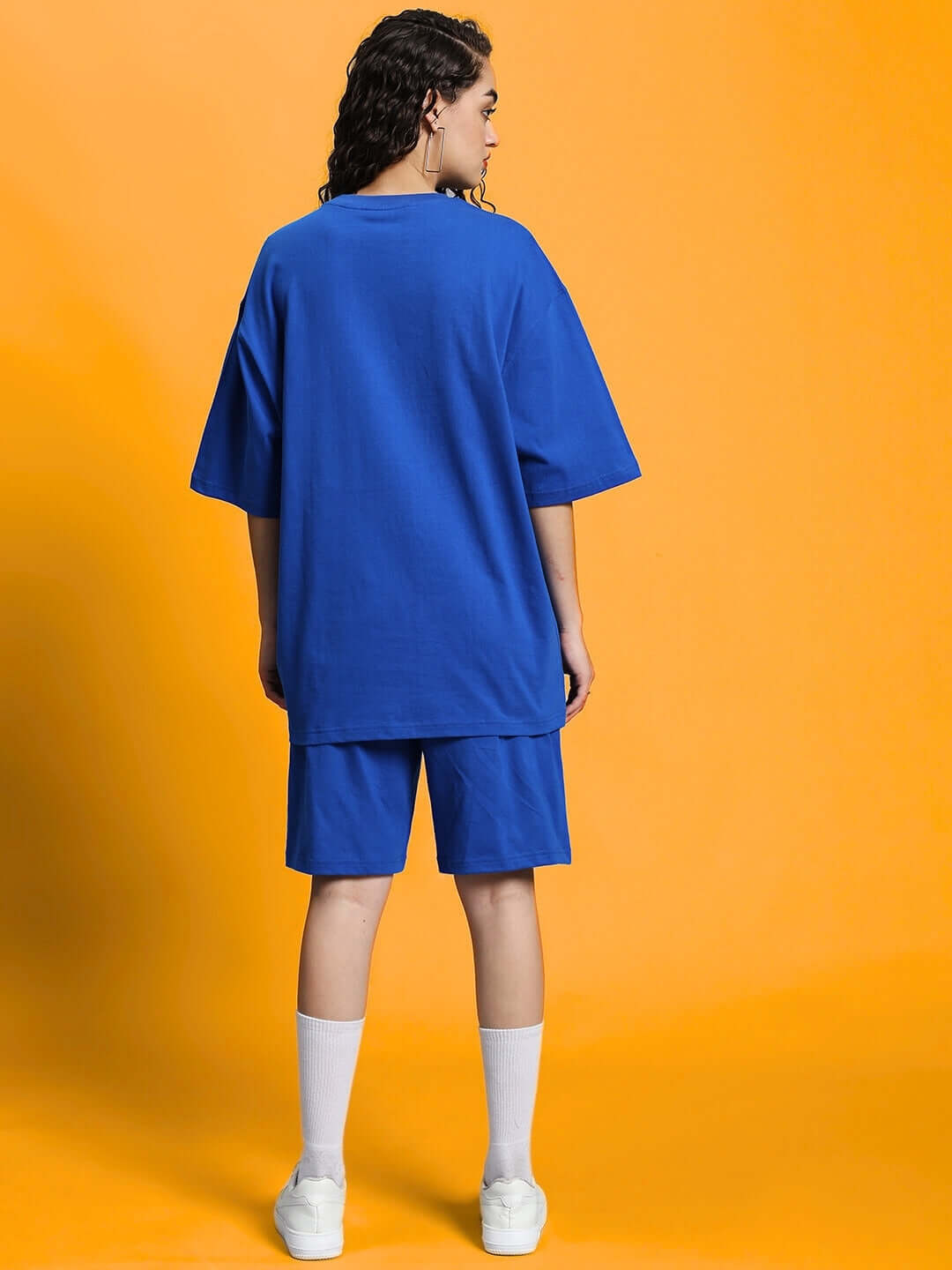 Back view of woman wearing WOMEN'S OUTLOOK SUMMER CO-ORD SHORTS SET ROYAL BLUE, showing relaxed fit t-shirt and shorts on orange background.