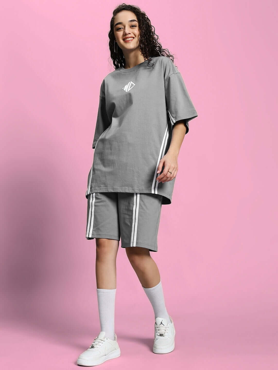 Woman wearing the WOMEN'S OUTLOOK SUMMER CO-ORD SHORTS SET GREY, featuring a relaxed-fit t-shirt and matching shorts against a pink background.