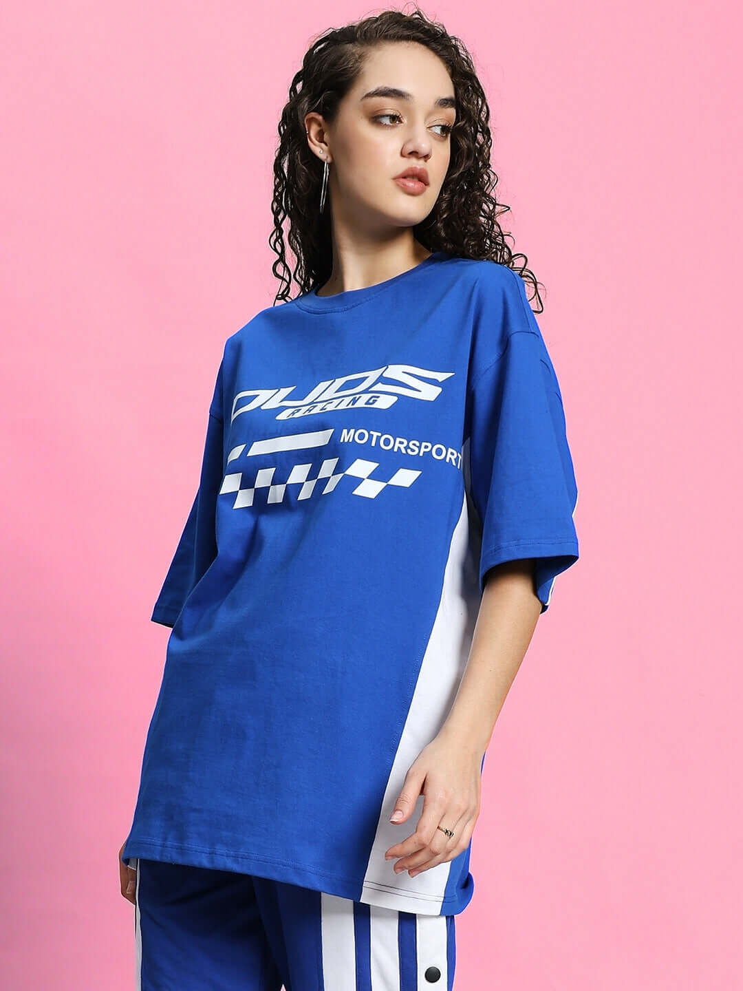 Woman wearing an oversized blue T-shirt with a motorsport graphic, made of premium cotton fabric, set against a pink background.