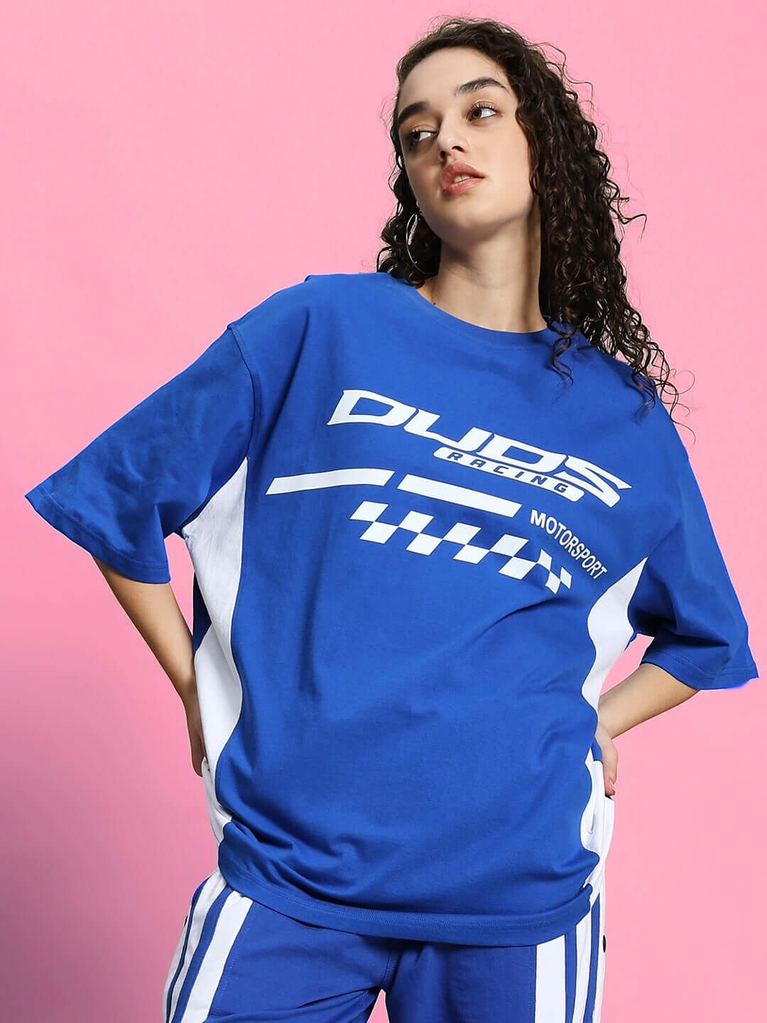 Woman wearing oversized blue t-shirt with graphic design, standing against a pink background.
