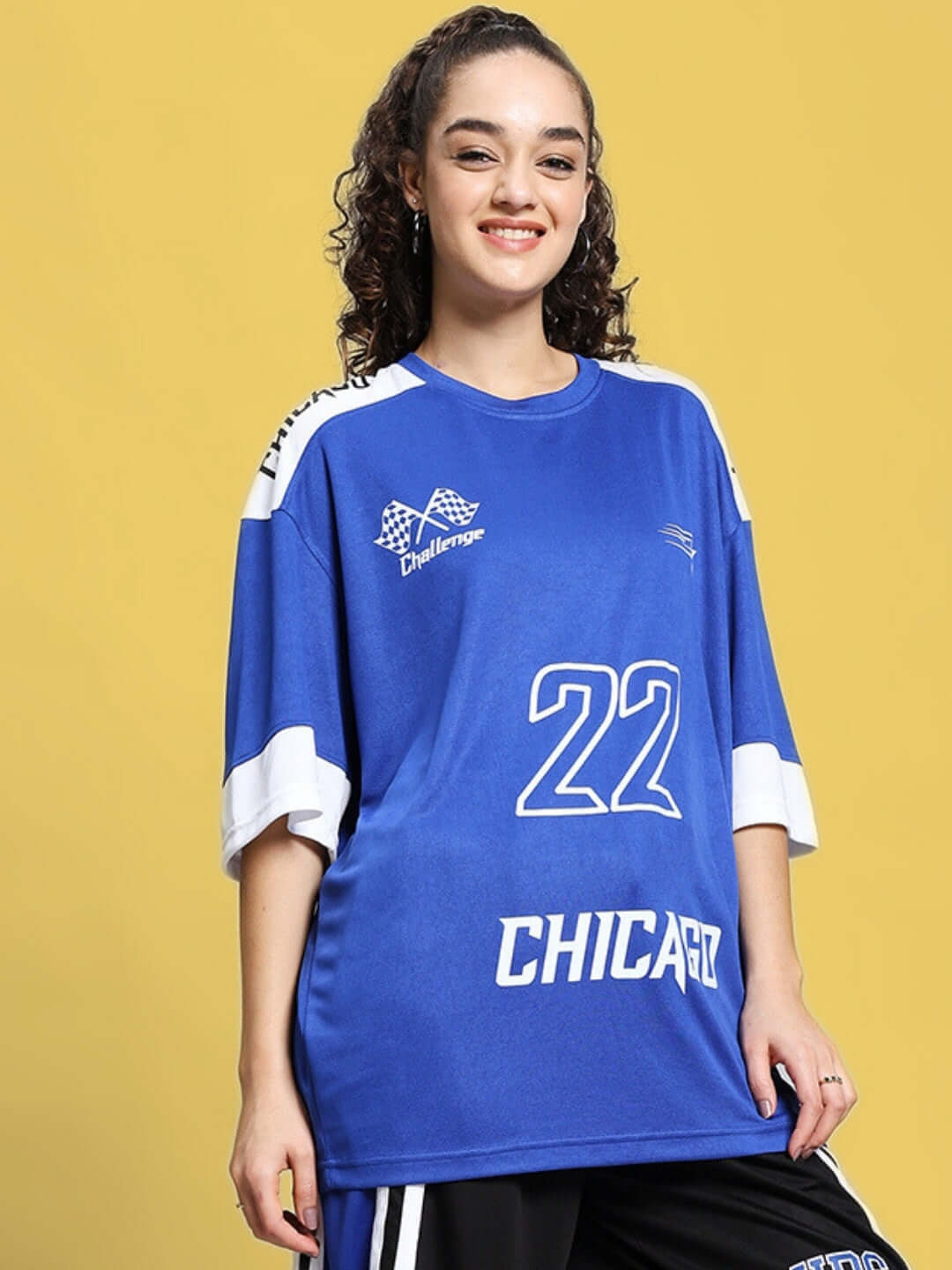 Woman wearing a royal blue oversized T-shirt with 'Chicago 22' print, styled casually on a yellow background.