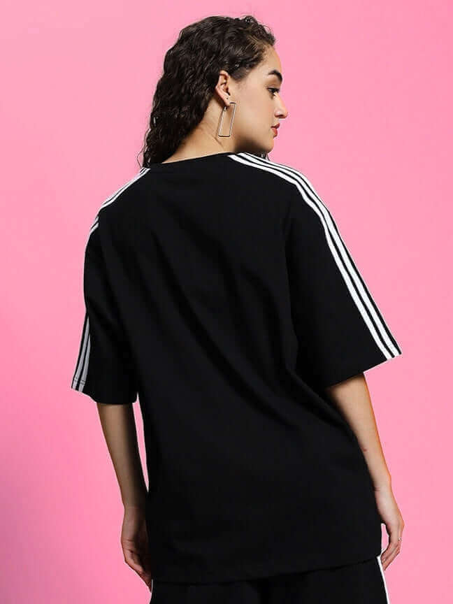 Woman wearing black oversized classic t-shirt with striped shoulders, made from premium cotton fabric. Perfect for casual style.