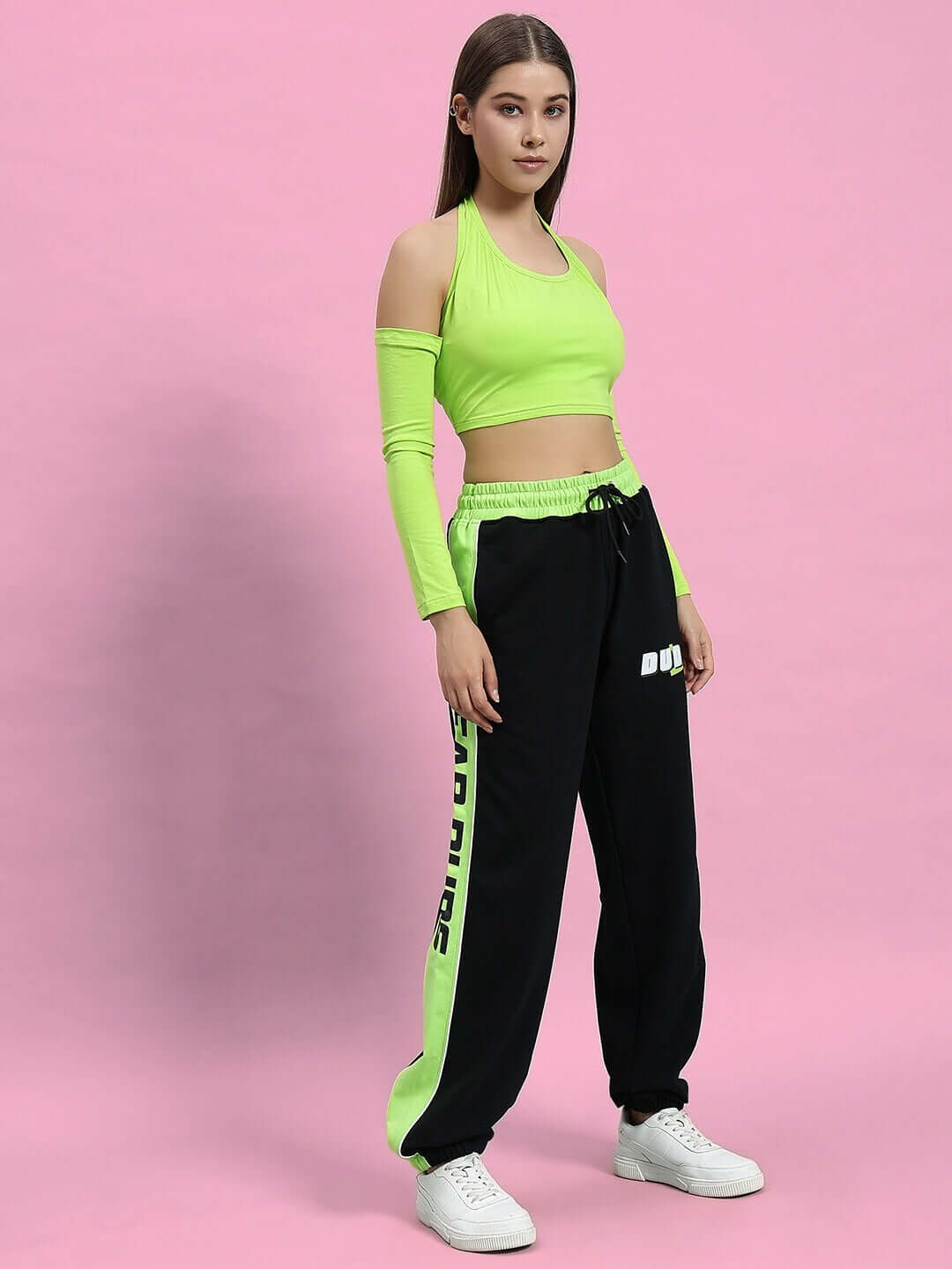 Woman modeling women's Peppy joggers in black and neon green with a matching top on a pink background.