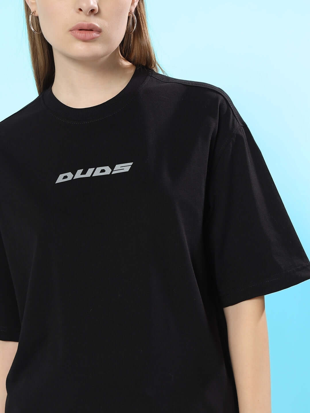 Model wearing a black oversized t-shirt with reflective text, showcasing modern streetwear fashion against a blue background.