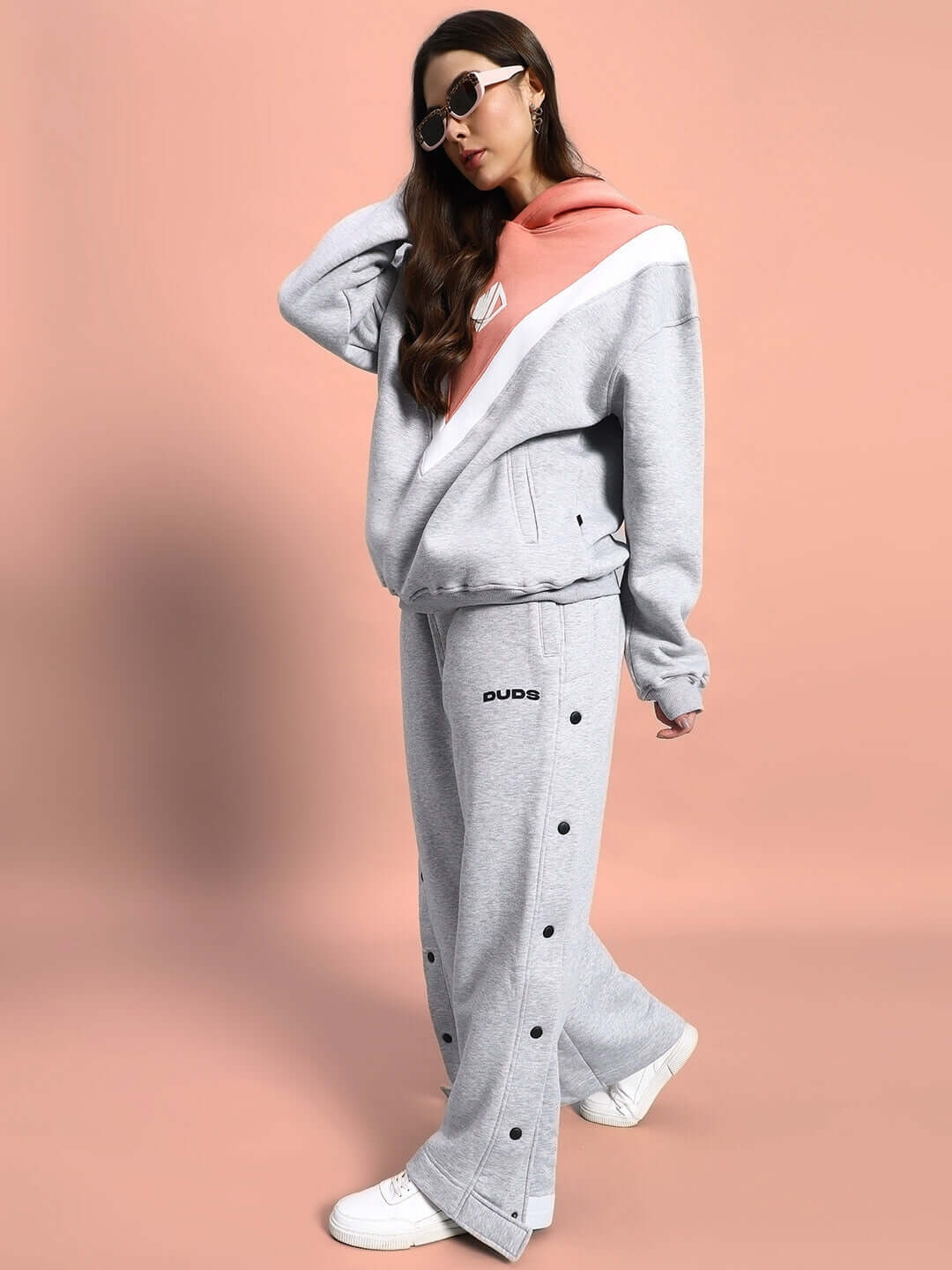 Woman wearing WOMEN POLAR COLORBLOCK HOODIE GREY PEACH with stylish sunglasses against a peach backdrop.