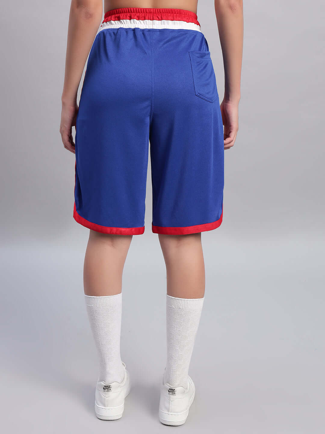 Back view of Women's Portia Regular Fit Shorts in royal blue, featuring red trim and pocket detail, styled with sneakers and socks.