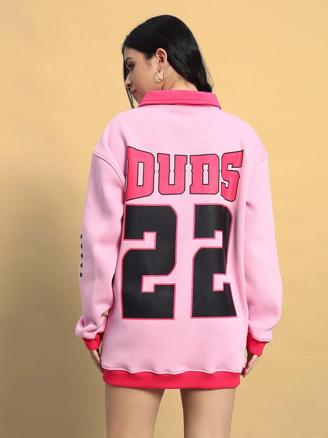 Woman wearing pink WOMEN'S POWER22 sweatshirt dress with DUBS 22 printed on the back, standing against a beige background.
