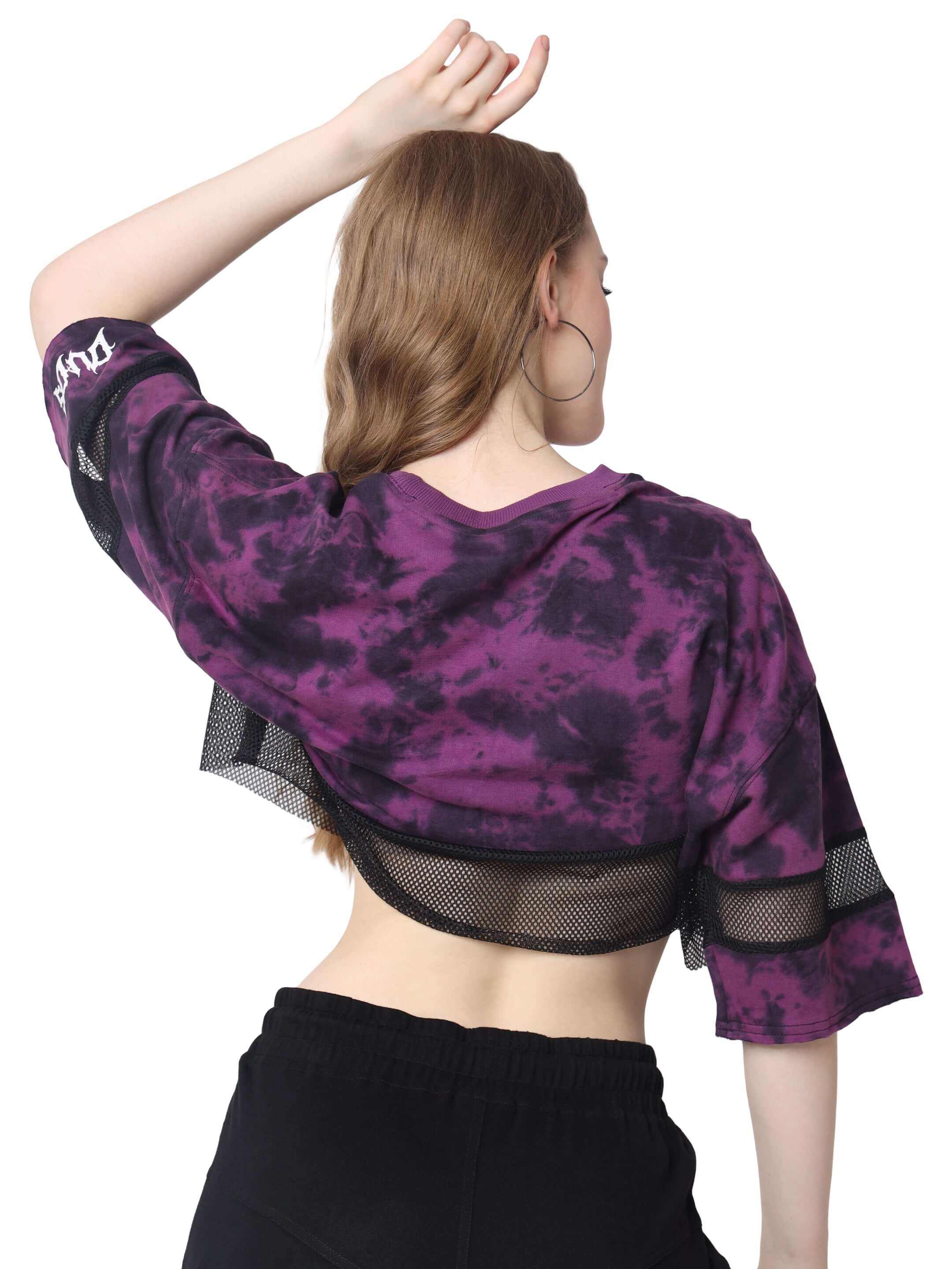 Back view of a woman wearing a purple tie-dye oversized cropped T-shirt with mesh details, made of premium cotton blend.