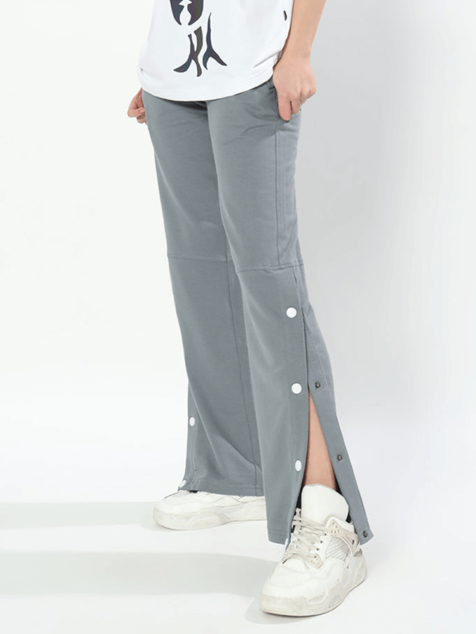 Woman wearing grey racer joggers with buttoned slits, paired with white sneakers, showcasing versatile and stylish comfort wear.
