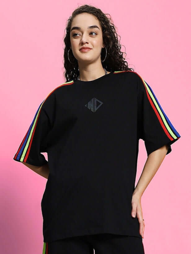 Model wearing women's black oversized t-shirt with rainbow stripes, made of premium cotton fabric, shown on a pink background.